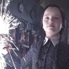 Dark-haired pale girl in black dress with white details in dimly lit room