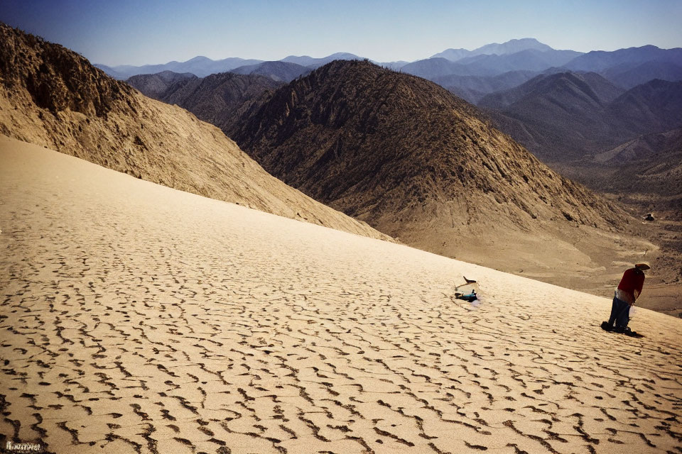 Person in Red Shirt with Sled on Sandy Slope Overlooking Desert Landscape