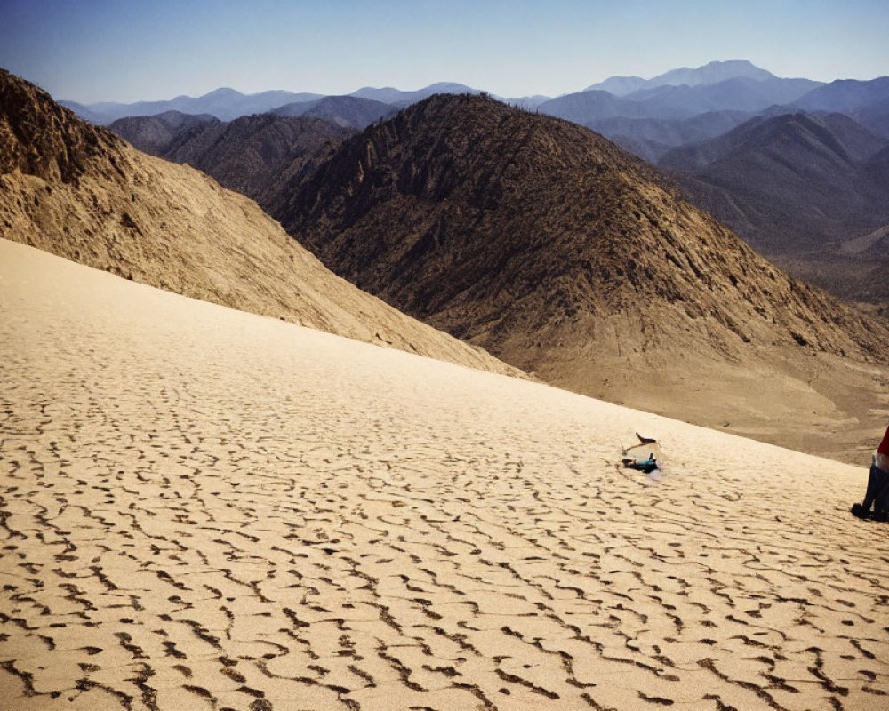 Person in Red Shirt with Sled on Sandy Slope Overlooking Desert Landscape