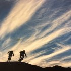 Cyclists on rocky terrain under vibrant sunset sky