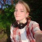 Blonde person in pink and white jacket posing in forest with sunlight.