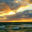 Colorful sunset scene with wavy ocean and dramatic clouds