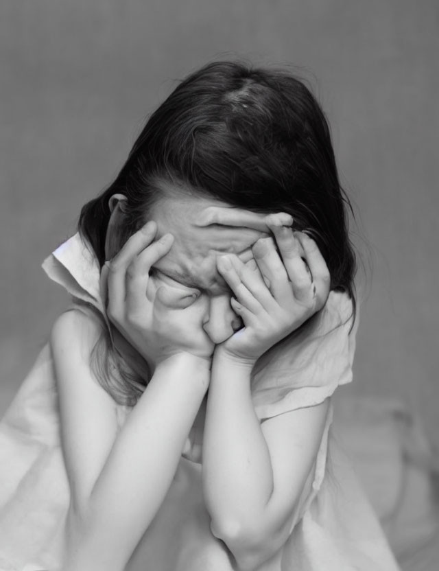 Monochrome image of distressed child with hands covering face