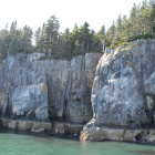 Watercolor painting of rugged cliff face above blue waters