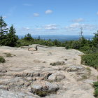 Colorful Landscape Painting with Patterned Rocks, Pine Trees, and Blue Mountains