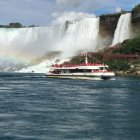 Tour boat with passengers near massive waterfall in choppy waters