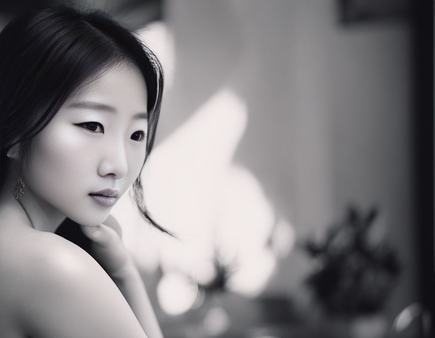 Monochrome portrait of pensive East Asian woman, looking sideways, with blurred backdrop