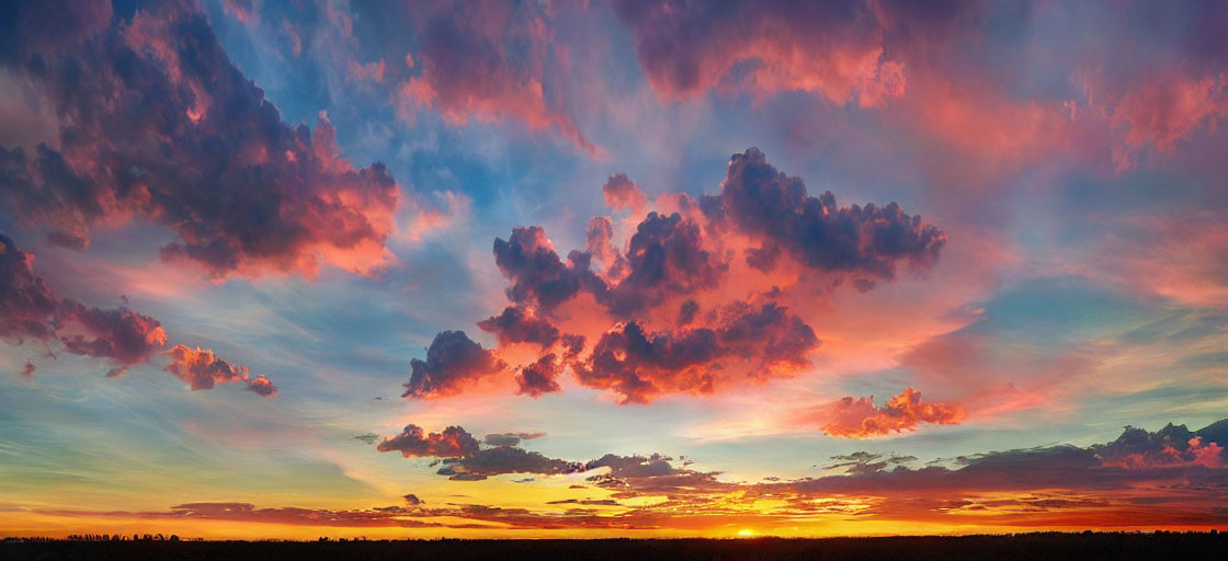 Vibrant sunset panorama with orange, red, and blue hues over silhouetted horizon