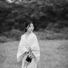 Monochrome image of woman in Japanese attire in field with blurred trees