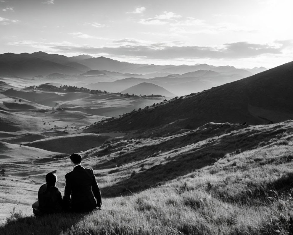 Scenic view of two individuals on grassy hill overlooking mountains