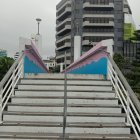 Weathered building with colorful peeling paint and greenery, concrete staircase under overcast sky