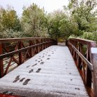 Snow-covered wooden bridge with glowing lanterns in winter scene.