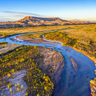 Colorful rural landscape with river, houses, and mountains under blue sky