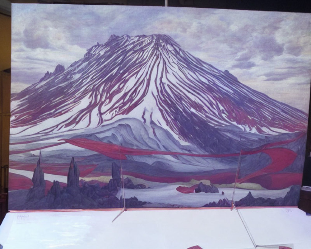 Snow-capped mountain with red streaks under cloudy sky and rocky terrain.