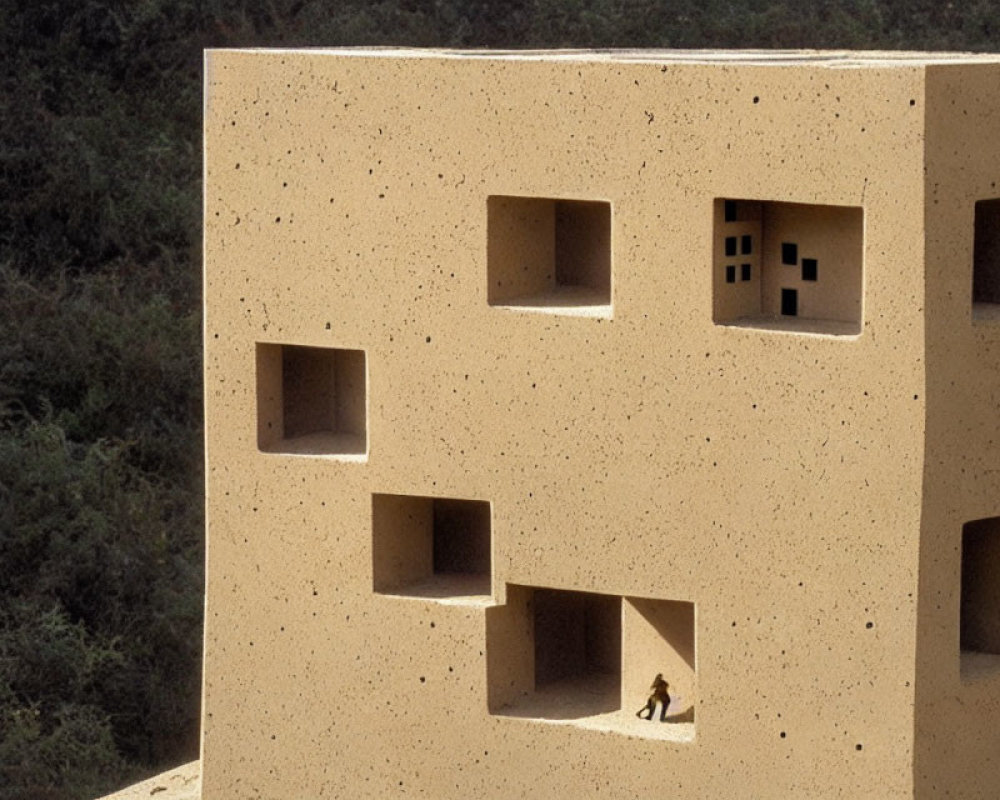 Person observed through large square windows of geometric sandy-textured building.