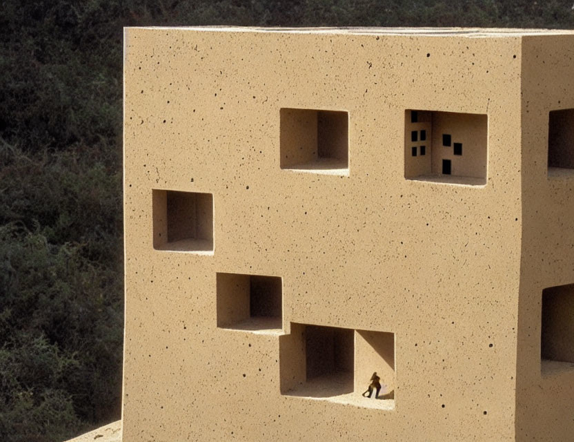 Person observed through large square windows of geometric sandy-textured building.