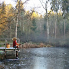 Young boy fishing on wooden dock by serene lake surrounded by trees and rocks