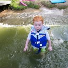 Red-Haired Toddler in Life Jacket Floats Near Rocky Edge