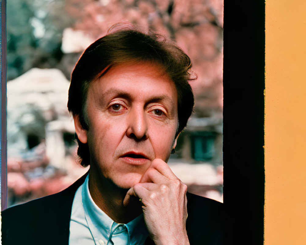 Contemplative man by window with pink blossoms, framed in vivid yellow and black.