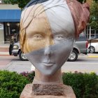 Large baby head sculpture with intricate features in city square, child with toy airplane.