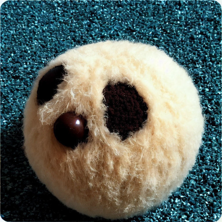 Round beige fluffy toy with dark center on blue textured surface