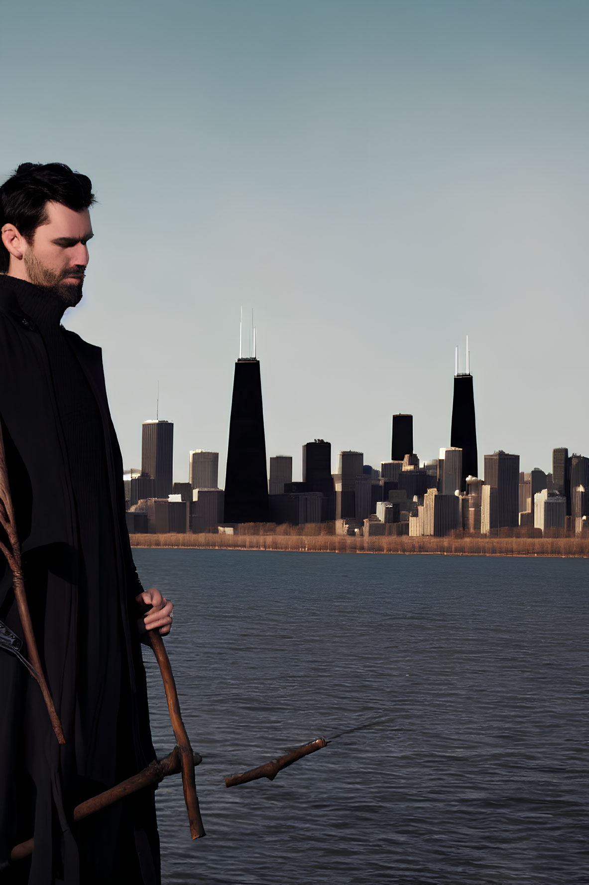 Man with staff by water and city skyline in clear sky