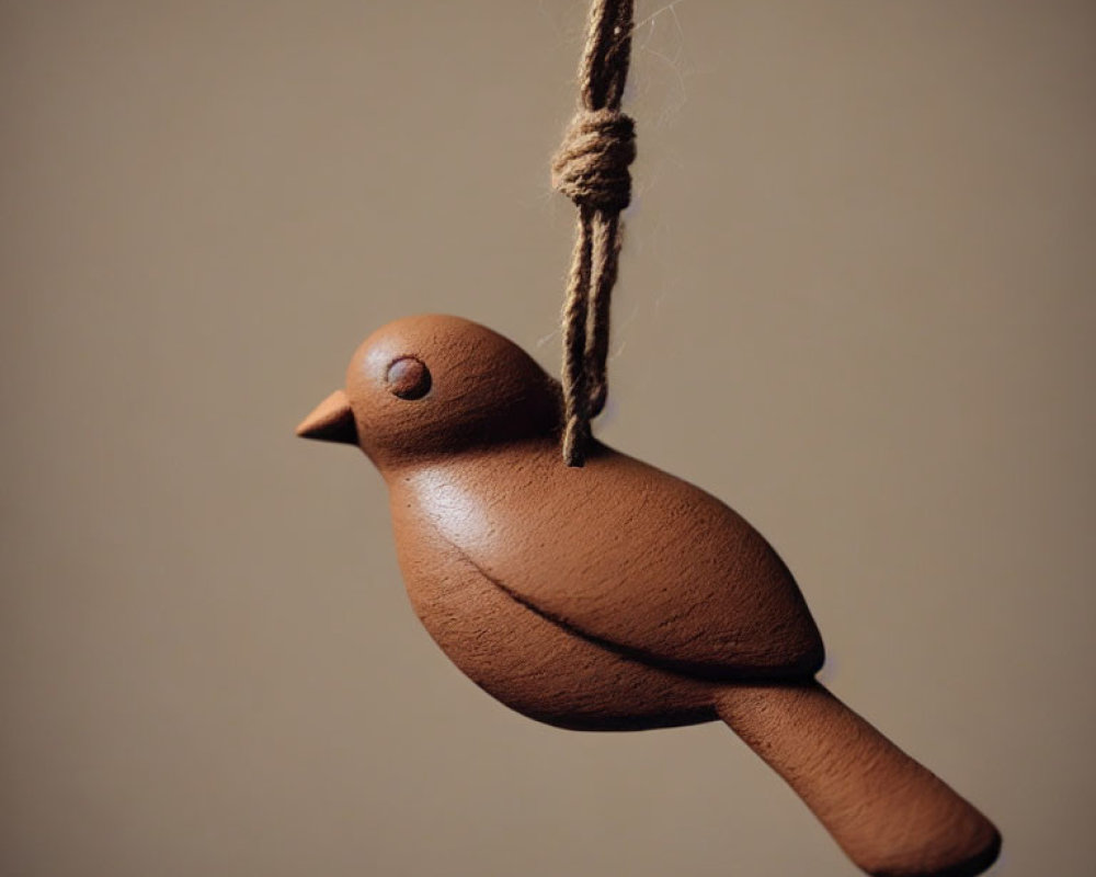 Wooden bird figure hanging on twine against neutral background