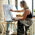 Bohemian woman painting colorful floral piece in bright room