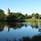 Tranquil lake scene with church, houses, and mountains under blue sky