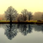 Tranquil autumn landscape with reflective lake and cottage under yellow sky