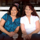 Two women with intricate tattoos and ornate clothing against a patterned backdrop, one in blue attire and