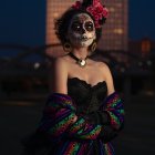 Woman with Day of the Dead makeup and floral headpiece on decorative backdrop.