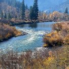 Mountainous landscape painting with river, autumn trees, and blue sky