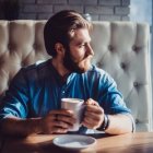 Middle-aged man with mustache in diner holding coffee cup, vintage cars outside