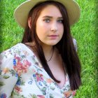 Portrait of woman with long brown hair, red lips, white hat, floral dress on green background