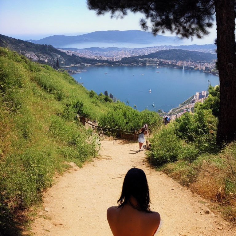 Dark-haired person gazes at scenic lake and hills under clear sky.