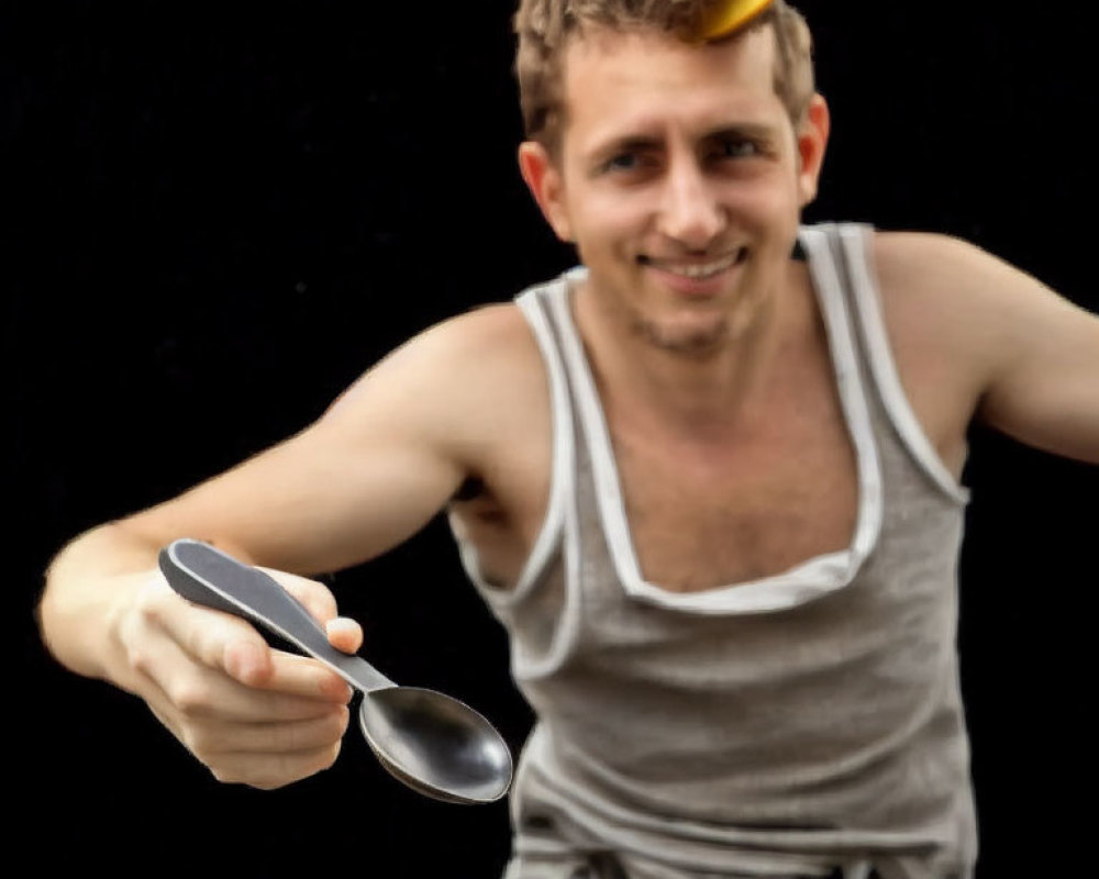 Person in white tank top balancing banana on head with spoon on black background