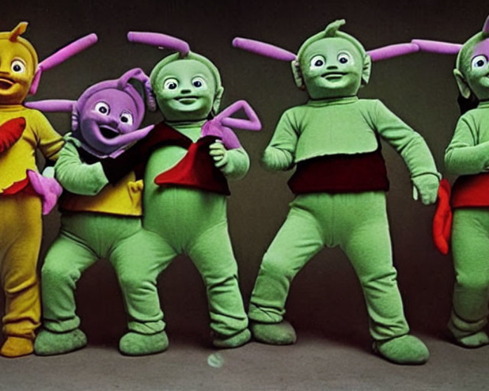 Four individuals in colorful costumes with antennae and smiling faces standing side-by-side