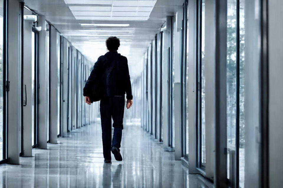 Man in dark suit walking down bright modern corridor with glass doors