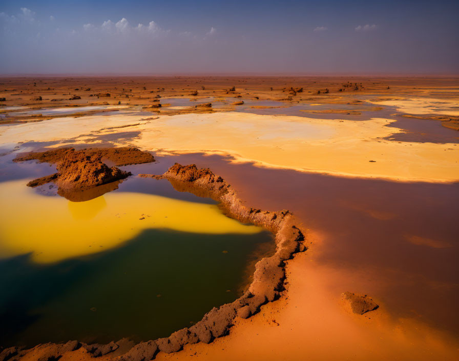 Vibrant yellow and green sulfur pools in sandy terrain under hazy blue sky