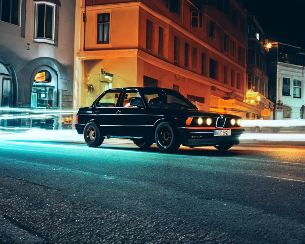 Vintage Black Car Parked on City Street at Night with Passing Vehicle Light Streaks