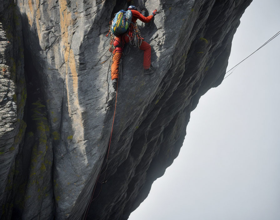 Climber in Red Gear Ascending Steep Rock Face with Ropes