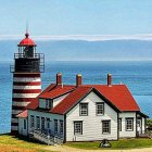 Miniature red and white lighthouse beside small red roofed house with mountain backdrop