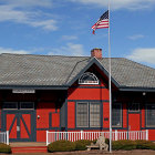 Rustic wooden building with flag and ox-drawn carts under moody sky