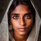 Woman with hood and intricate face patterns and luminous eyes