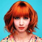 Vibrant orange-haired woman with bangs on turquoise background