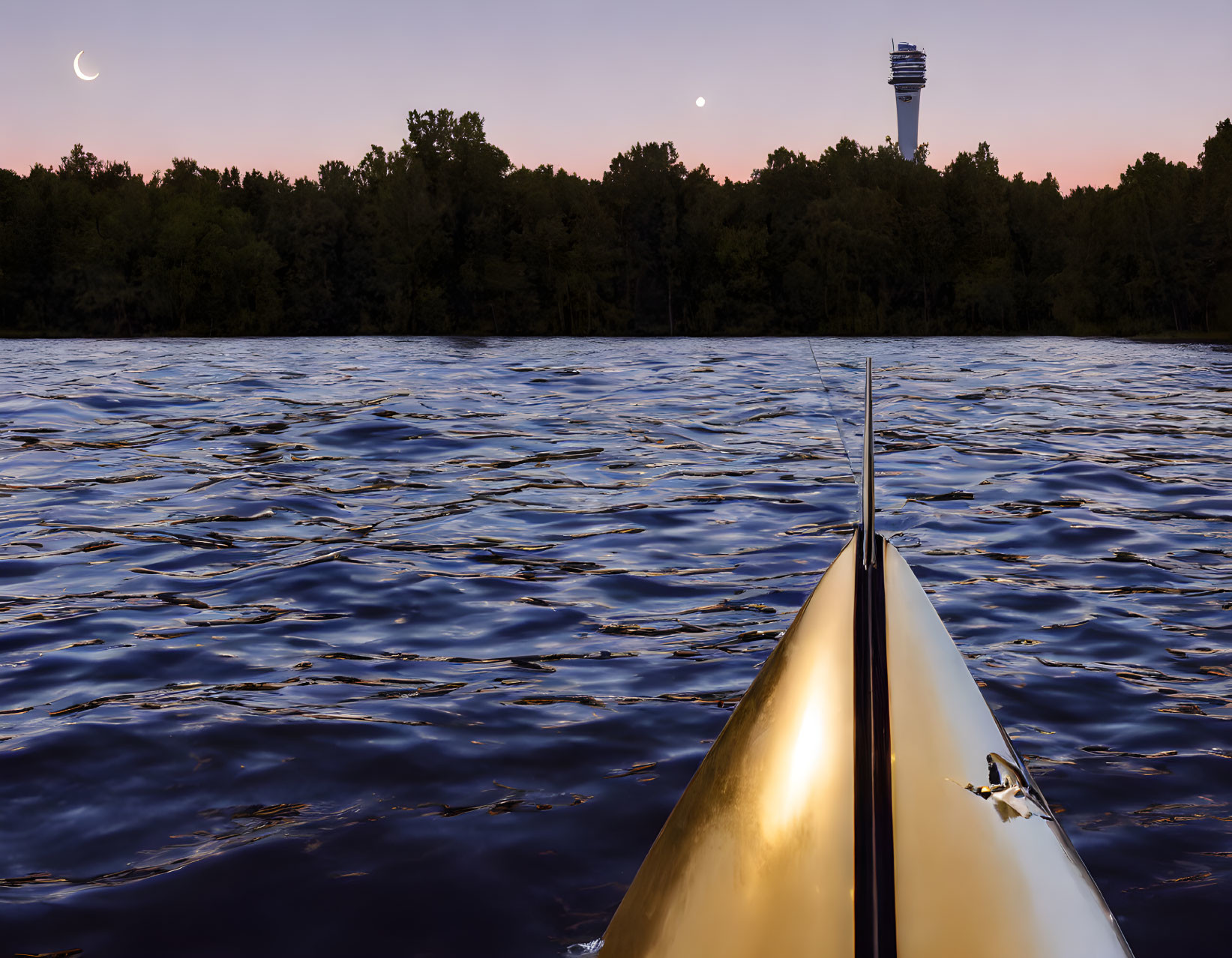 Kayak bow on water at twilight with crescent moon, trees, and distant tower