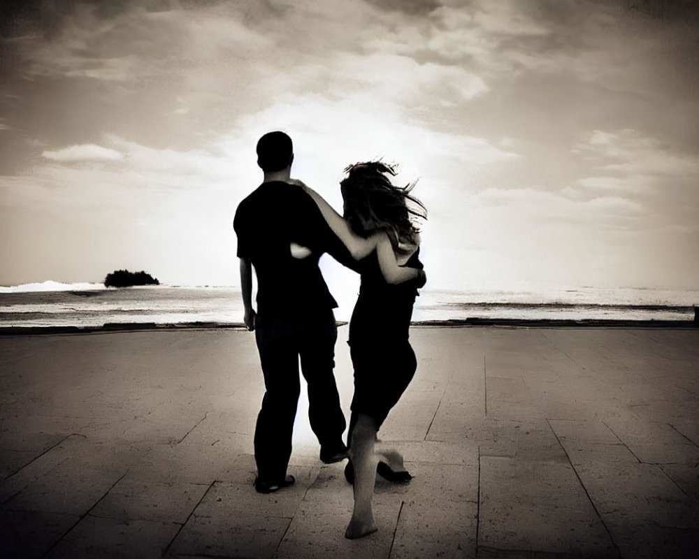 Silhouetted couple dancing by the sea under a cloudy sky