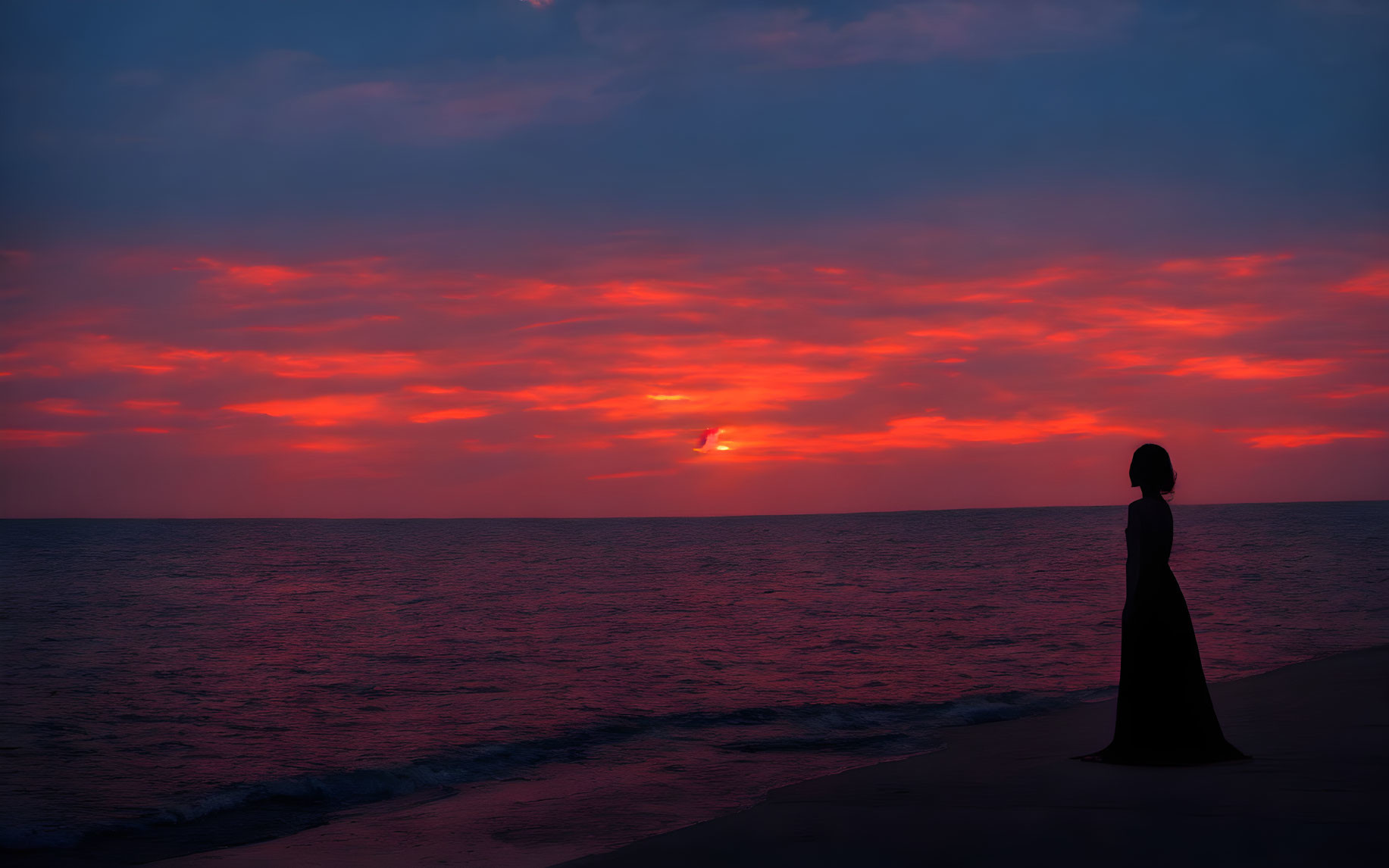 Silhouetted Figure by Sea Under Vivid Sunset Sky