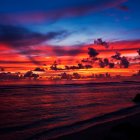 Silhouetted Figure by Sea Under Vivid Sunset Sky